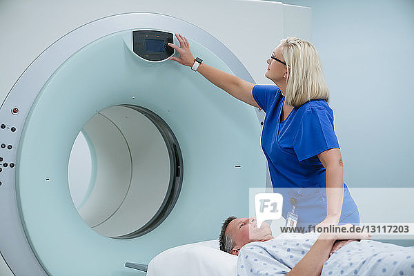 Nurse adjusting button on MRI Scanner while patient lying in examination room
