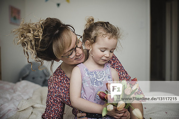 Tochter hält Tulpen  während sie zu Hause mit der Mutter im Bett sitzt