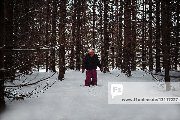 Girl looking up while standing on snow covered field in forest