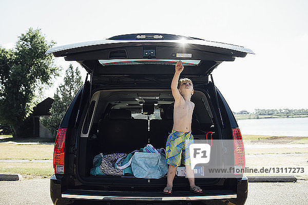 Junge ohne Hemd auf Kofferraum stehend