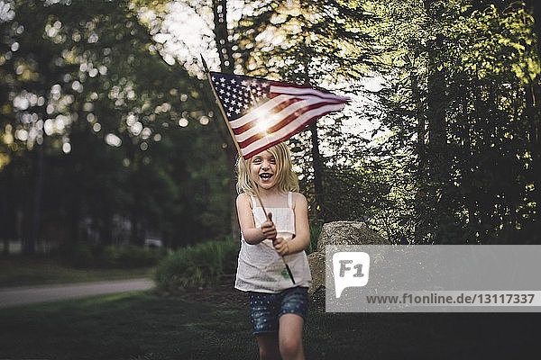 Cheerful girl with American flag running in yard during sunny day