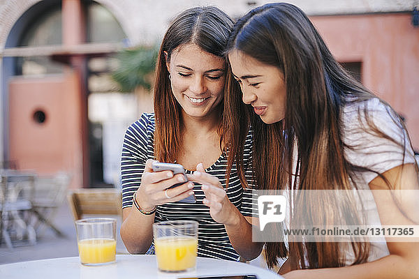Freunde benutzen Mobiltelefon  während sie im Straßencafé sitzen