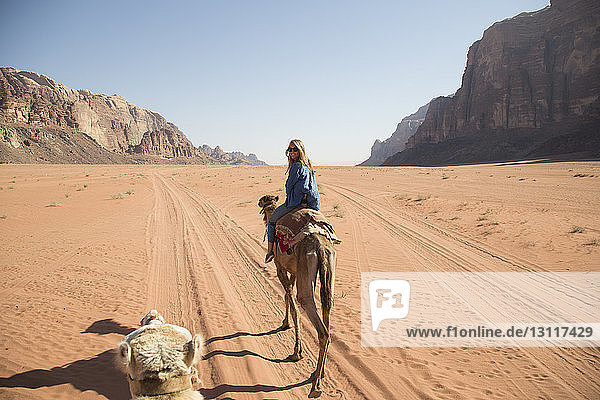 Female tourist looking over shoulder while riding on camel in desert