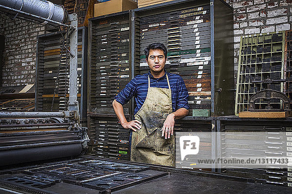 Portrait of worker standing by machinery at workshop