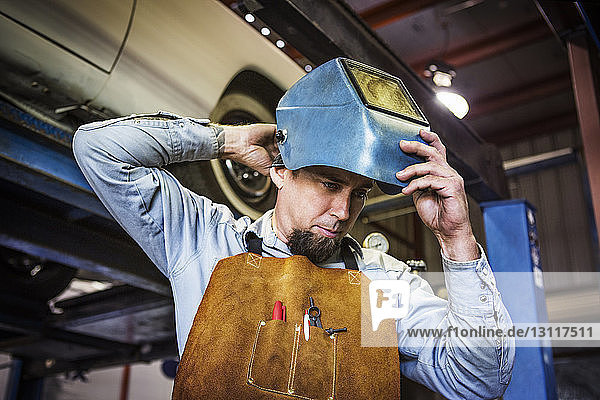 Mechaniker trägt einen Schweißerhelm  während er in einer Autowerkstatt steht