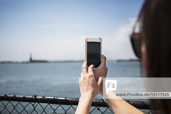 Frau fotografiert Fluss durch Smartphone gegen den Himmel