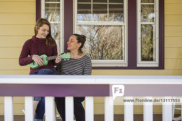 Glückliche Mutter schaut auf Gitarre spielende Tochter  während sie auf dem Balkon sitzt