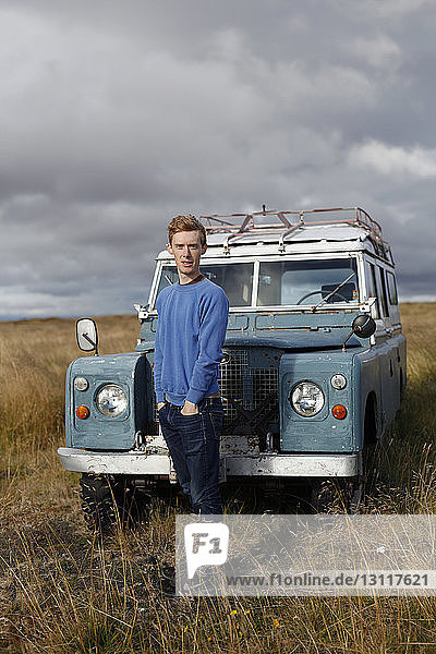 Portrait of confident man with hands in pockets standing against off-road vehicle against cloudy sky