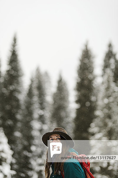 Seitenansicht einer Frau mit Rucksack  die im schneebedeckten Wald gegen den Himmel steht