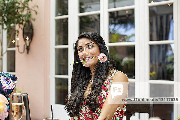 Schöne Frau hält Blume im Mund im Freiluftrestaurant