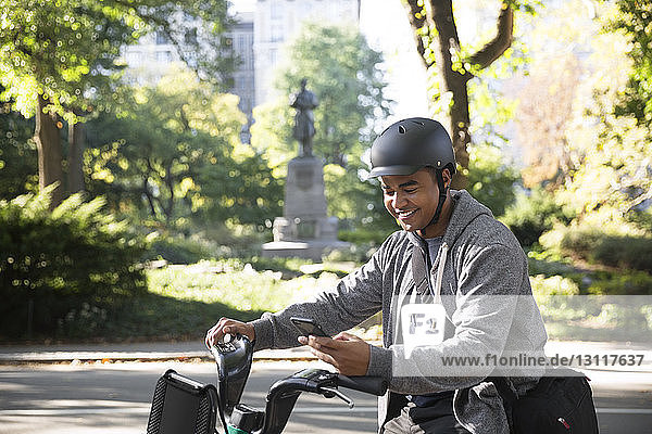 Smiling man using mobile phone while riding bicycle on city street