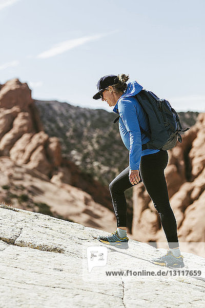 Side view of female hiker with backpack walking on mountain during sunny day