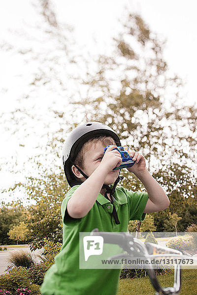 Boy photographing through camera while cycling at park