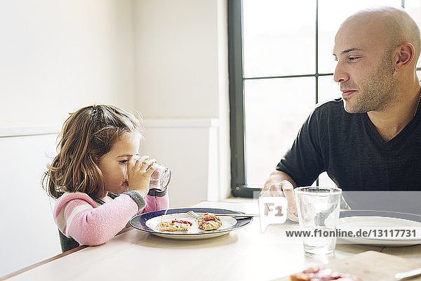 Man looking at daughter drinking water at table in home