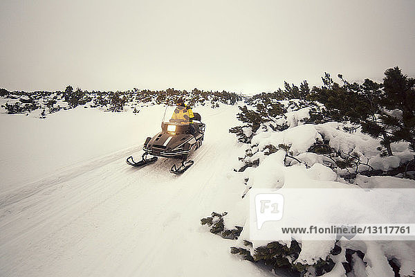 Man driving snowmobile on snowy field against sky