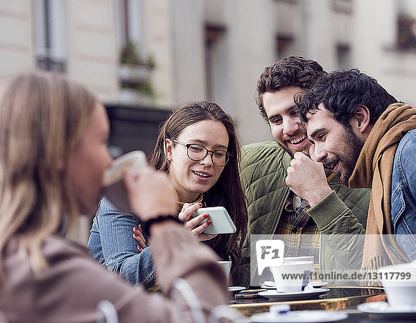 Glückliche Frau zeigt männlichen Freunden im Straßencafé ihr Smartphone