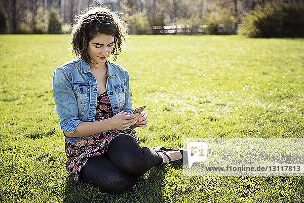 Frau benutzt Smartphone  während sie auf einem Grasfeld sitzt