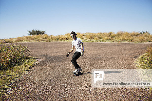 Mann fährt Skateboard auf Straße und Feld gegen klaren Himmel