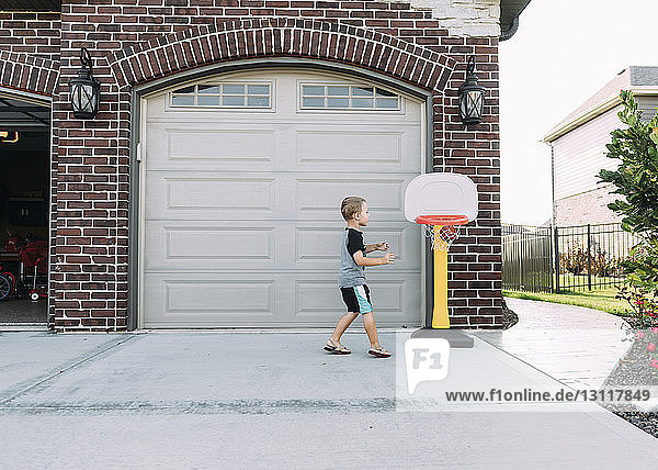 Glücklicher Junge spielt Basketball auf Einfahrt