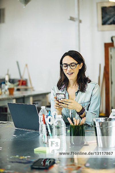 Glückliche Geschäftsfrau benutzt Smartphone bei der Arbeit im Büro
