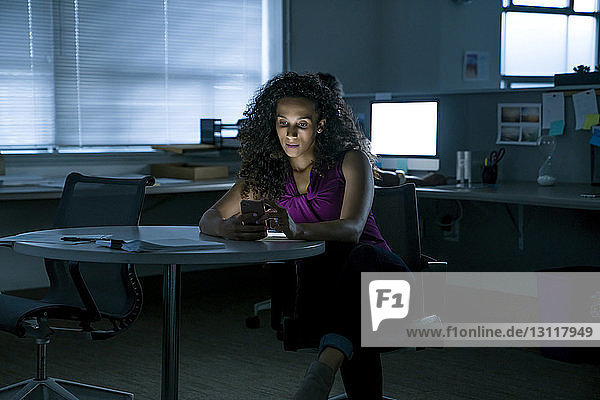 Geschäftsfrau benutzt Smartphone  während sie im Büro am Tisch sitzt