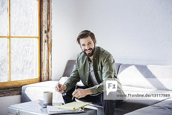 Porträt eines lächelnden Geschäftsmannes  der in einem Buch schreibt  während er im Kreativbüro sitzt