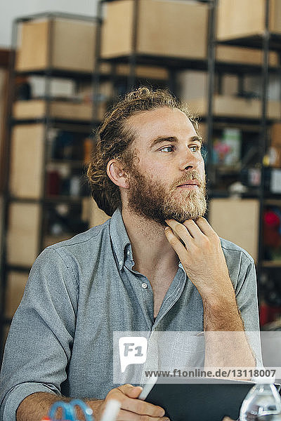 Thoughtful businessman holding tablet computer in office