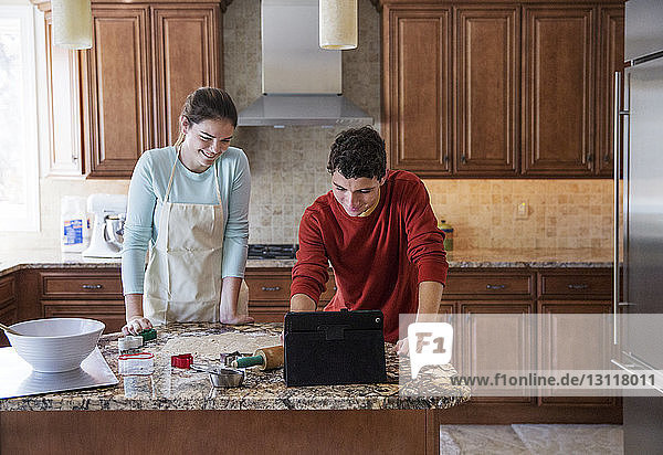Happy siblings using laptop computer in kitchen at home