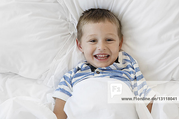 Portrait eines fröhlichen Jungen  der zu Hause auf dem Bett liegt