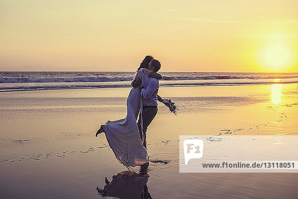 Neuvermähltes Paar umarmt sich am Strand vor klarem Himmel bei Sonnenuntergang
