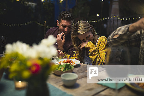 Glückliches Paar sitzt am Tisch  während es mit Freunden zu Abend isst