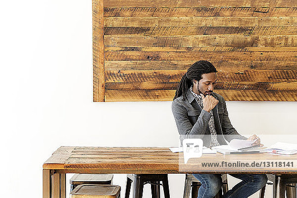 Junger Geschäftsmann analysiert Dokumente  während er im Kreativbüro sitzt