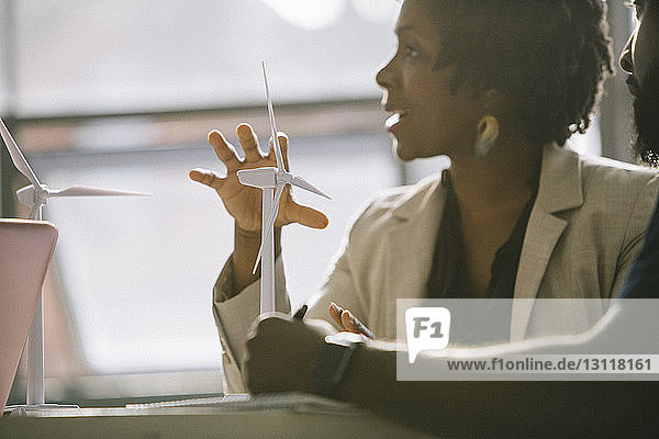 Businesswoman explaining over wind turbine models while sitting with colleague in office