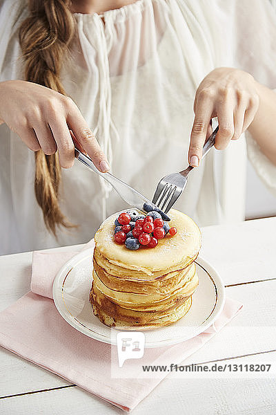 Midsection of woman eating pancakes on table while sitting at home