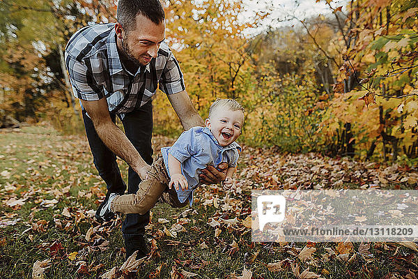 Father playing with son while standing on grassy field in forest during autumn