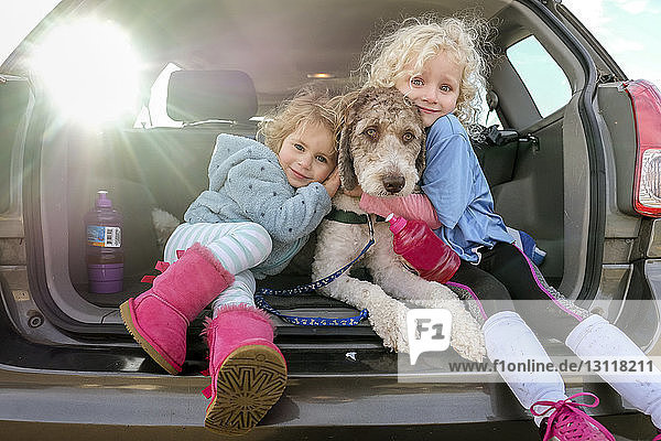 Porträt von lächelnden Schwestern  die einen Hund umarmen  der im Kofferraum eines Autos sitzt