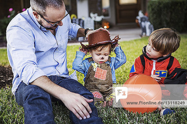 Father assisting son to wear cowboy hat while sitting on grass at backyard