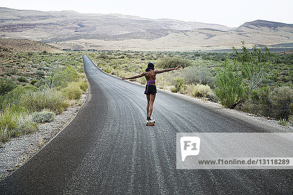 Rear view of woman skateboarding on road amidst field