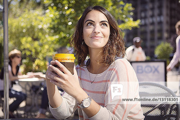 Nachdenkliche Frau hält Einweg-Kaffeetasse im Straßencafé
