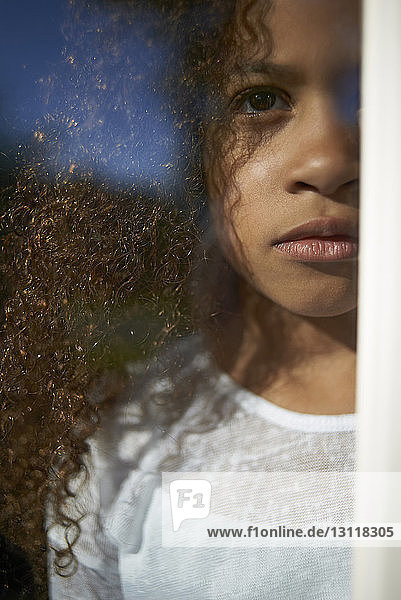 Mädchen schaut weg  während sie zu Hause durch Fensterglas gesehen wird