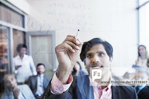 Businessman writing on glass wall and explaining during meeting in office