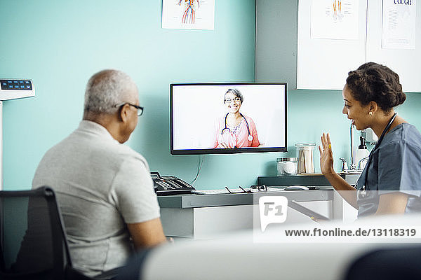 Videokonferenz einer Ärztin mit einer Kollegin  während sie mit dem Patienten in der Klinik sitzt