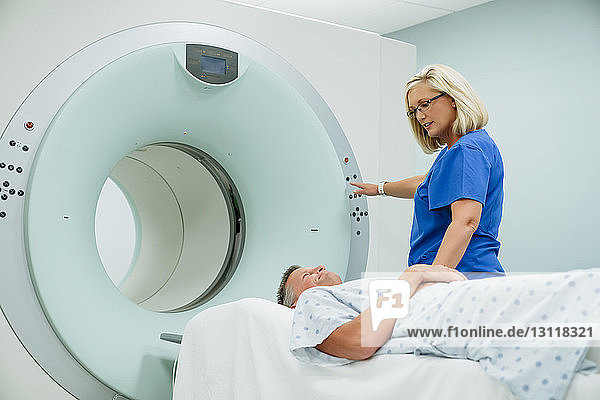 Krankenschwester sieht den Patienten auf dem MRT-Scanner liegend an  während sie im Untersuchungsraum den Startknopf drückt
