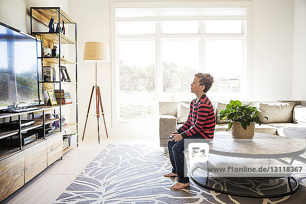 Boy sitting on table and playing video game at home
