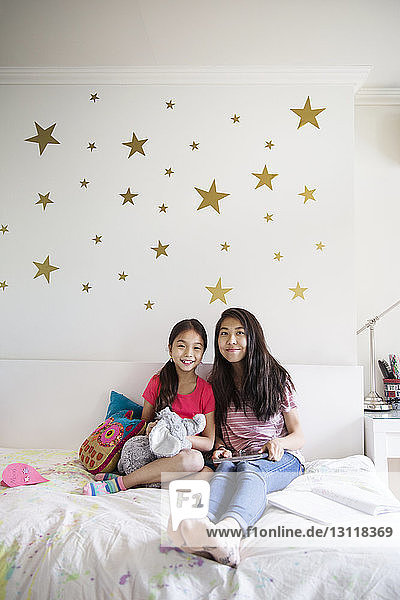 Portrait of smiling sisters sitting on bed at home