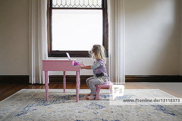 Side view of girl playing toy piano against window at home