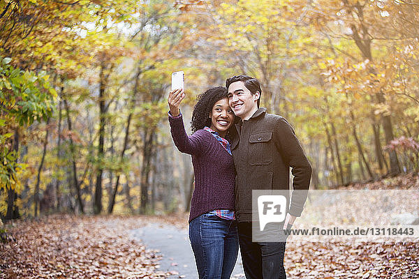 Happy couple taking selfie while standing on footpath in forest