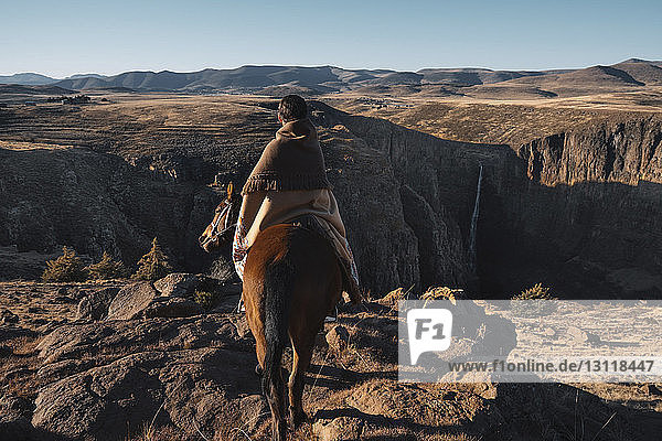 Rückansicht einer Frau  die auf einem Pferd am Berg reitet  bei klarem Himmel