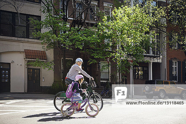 Side view of mother and daughter riding bicycles on street