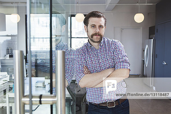 Portrait of confident businessman standing arms crossed in creative office